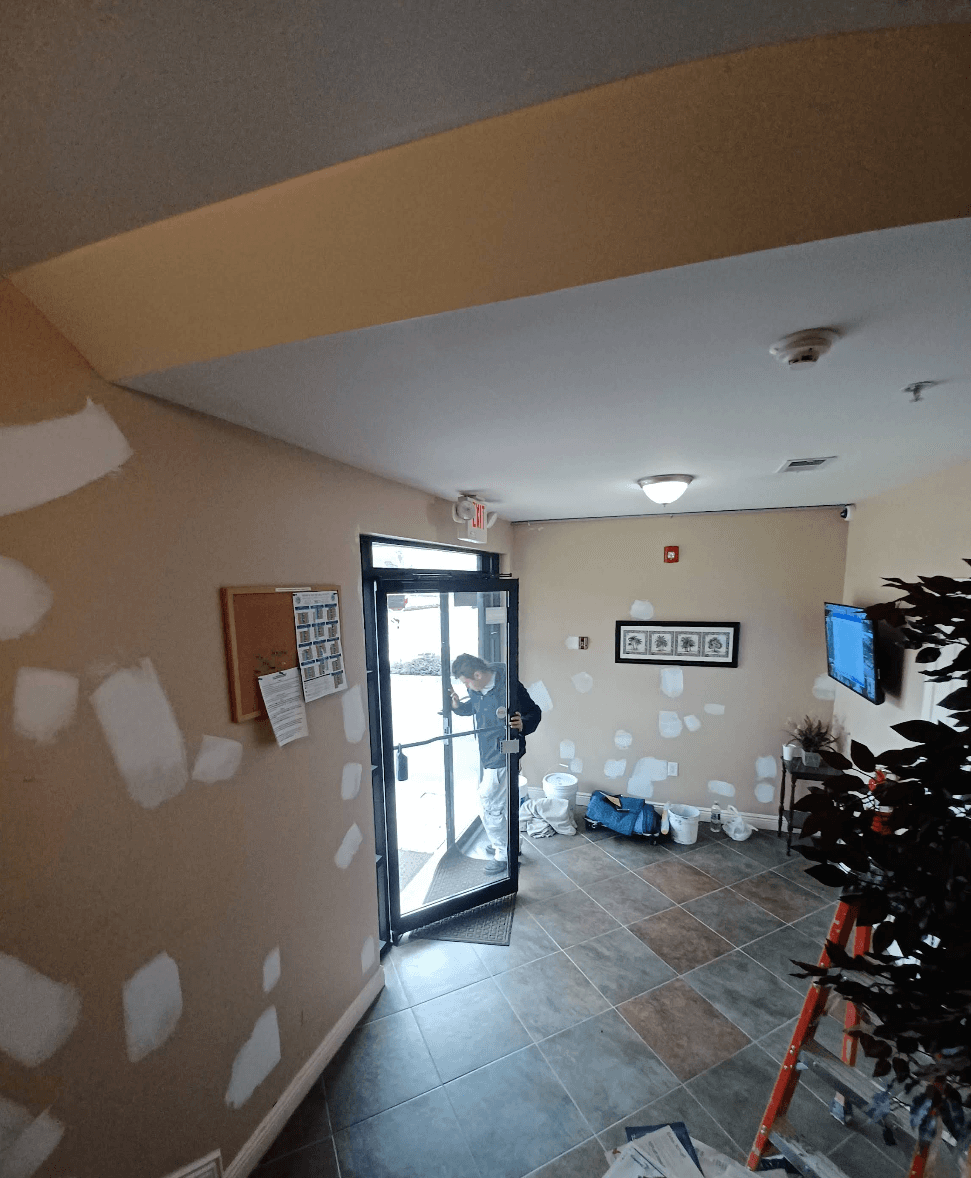 Man at a glass door in a lobby with white repair patches on tan walls.