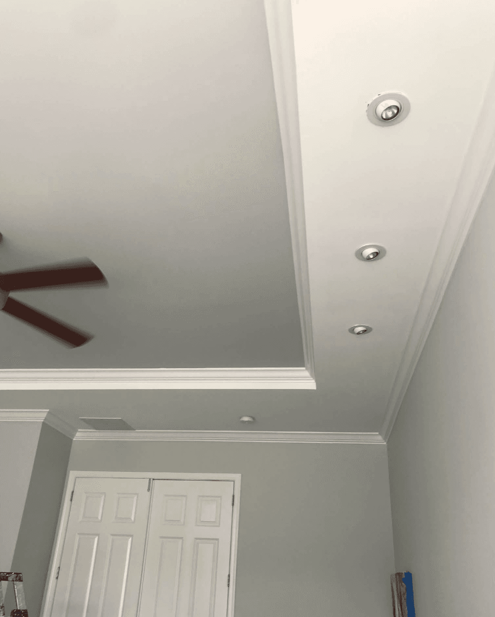 Grey tray ceiling with white crown molding, recessed spotlights, and a spinning ceiling fan.