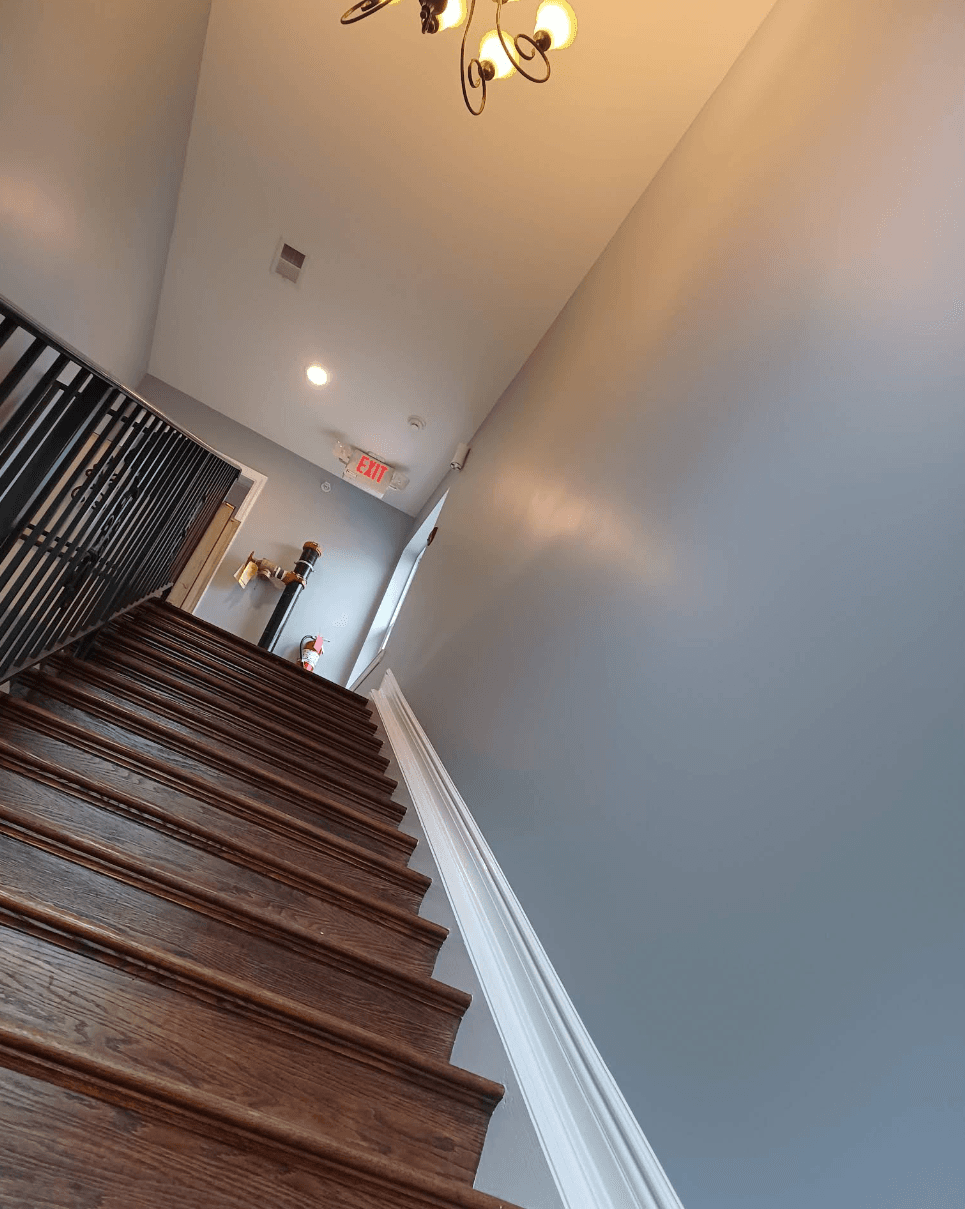 Tilted view of dark wooden stairs and black metal railing leading to an exit sign.