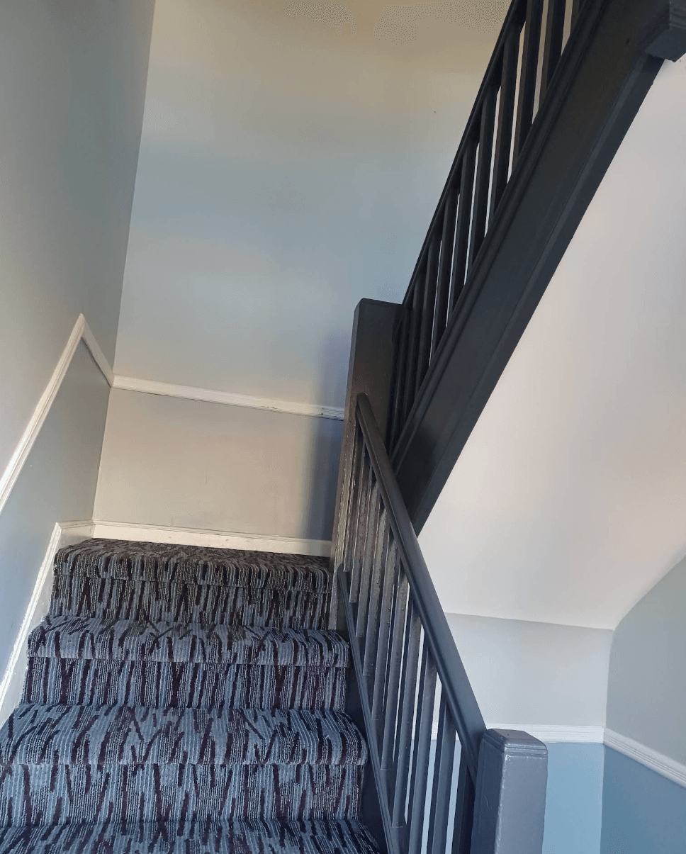 Staircase with striped purple and grey carpet, dark wooden banister, and light grey painted walls.