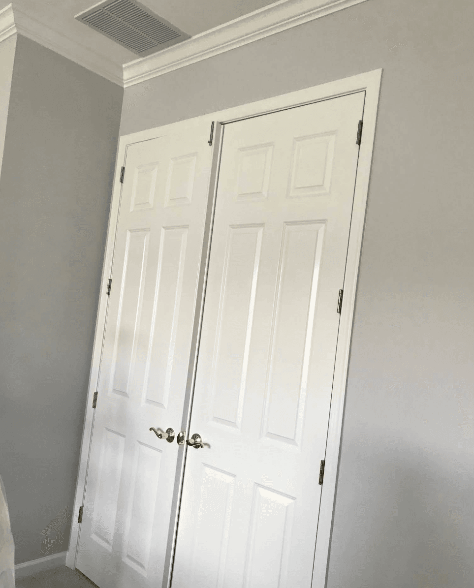 White six-panel double doors with gold hardware set against a light gray interior wall.