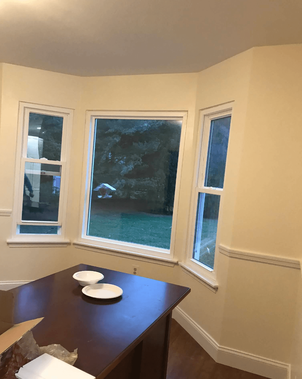 Bay window overlooking a yard at dusk, with white plates on a dark wooden table.